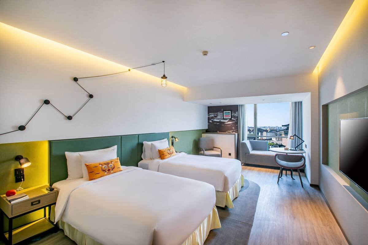 Hotelkamer met twee bedden, een bureau, een stoel, een televisie en een balkon met uitzicht over de stad.