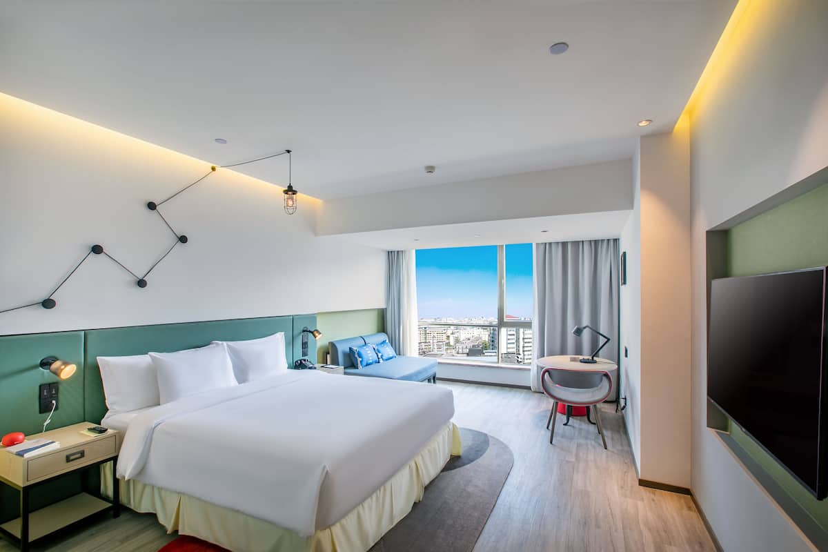 Een moderne hotelkamer met een groot bed, een bureau, een stoel, een televisie en een raam met uitzicht op de stad.
