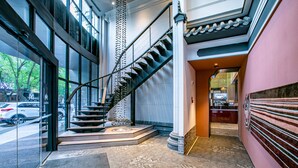 Un hall d’hôtel moderne avec une entrée en verre, un escalier en colimaçon et un comptoir d’accueil.