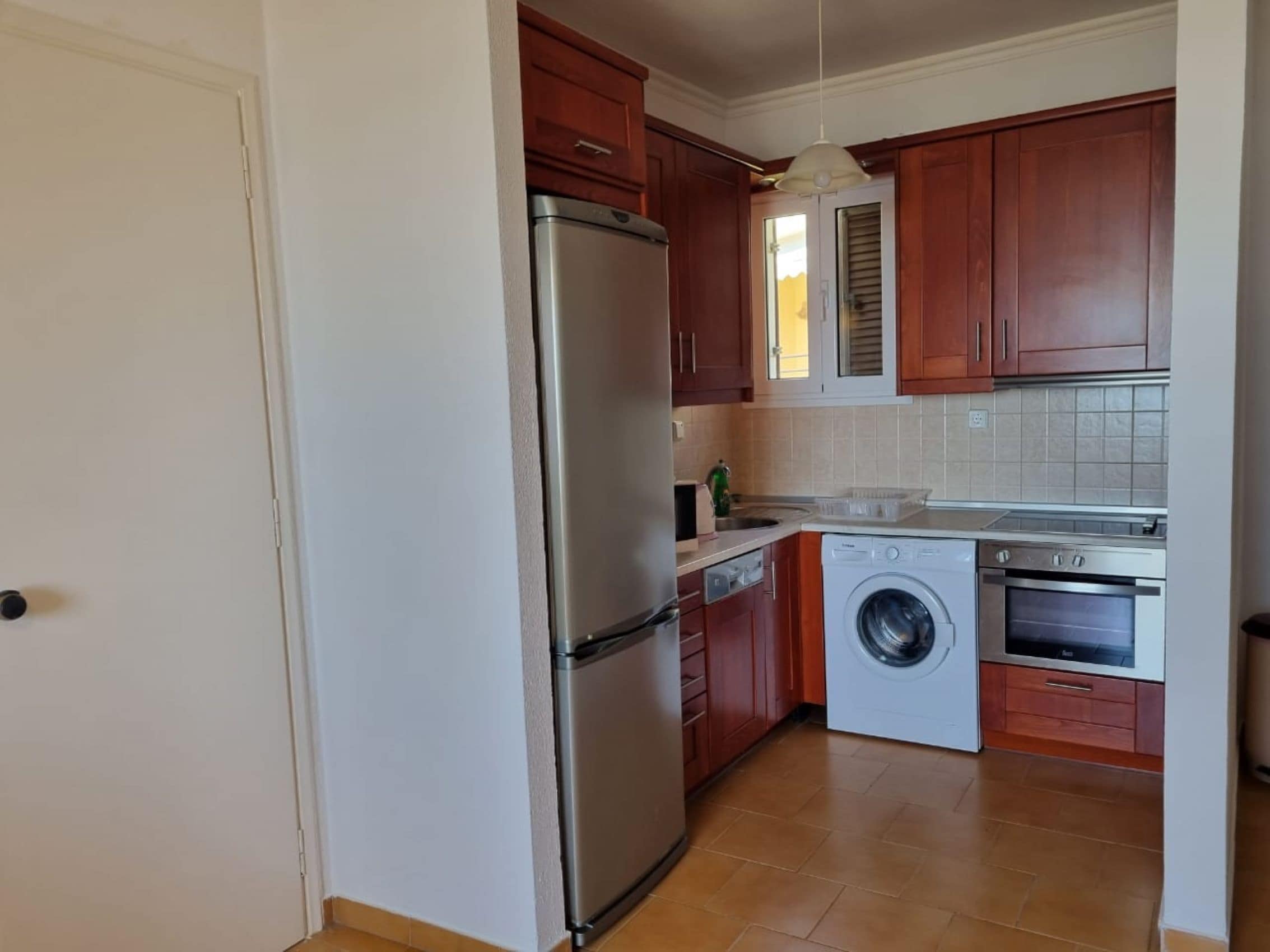 A compact kitchen with a stainless steel refrigerator, a washing machine, and an oven.