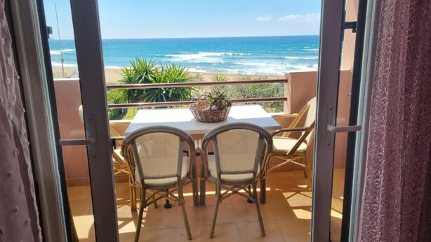 An open balcony with a table and chairs facing the ocean.