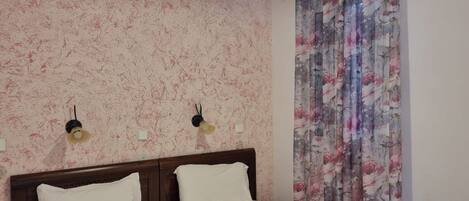 A room with two beds, a wooden headboard, a ceiling light fixture, and floral curtains.
