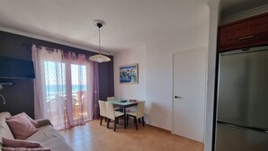 A compact living space with a sofa, dining table, chairs, a refrigerator, and a door.