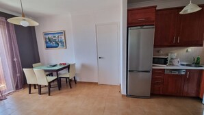 A compact kitchen with a refrigerator, microwave, and sink. There is a dining table with chairs and a painting on the wall.