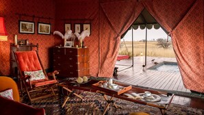 Une pièce avec un papier peint à motifs rouges, un meuble en bois, un fauteuil rouge, une table en bois avec un plateau, et une vue sur un jacuzzi et le paysage, visible à travers de grandes fenêtres.
