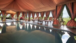 Un espace piscine intérieur luxueux, doté d’un sol réfléchissant, de grandes fenêtres avec rideaux et de plusieurs fauteuils confortables.