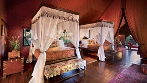 Un lit à baldaquin à quatre poteaux, surmonté d’une couverture à motifs floraux, une commode en bois et un fauteuil en cuir rouge.