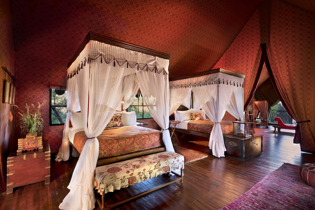 A four-poster canopy bed with a floral bedspread, a wooden chest of drawers, and a red leather armchair.