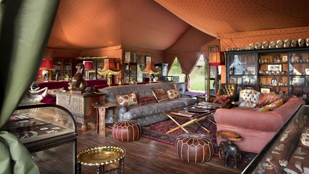 Un salon spacieux avec un plafond haut, un grand canapé, une table basse et une bibliothèque remplie d’objets décoratifs.