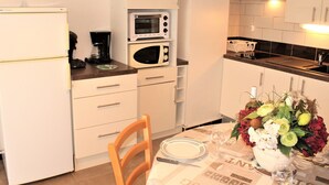 Une cuisine compacte équipée d’un réfrigérateur, d’un four à micro-ondes, d’une machine à café et d’une table à manger agrémentée d’un vase de fleurs.