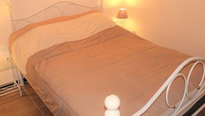 Un lit avec un cadre en métal blanc, une couverture beige et une lampe de chevet.