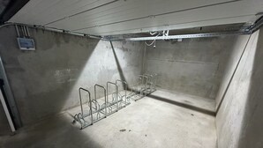 Une pièce en béton avec un support métallique pour vélos et une petite boîte électrique fixée au mur.