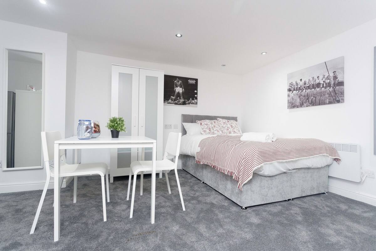 Ein modernes Schlafzimmer mit einem grauen Bett, weißen Möbeln und zwei schwarz-weißen Postern an den Wänden.