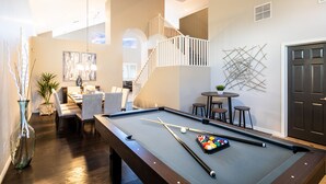 A pool table with pool cues and balls, a staircase, a dining area with chairs and a table, and a door. - Prime Location, Heated Pool, Fun Game Room, Putting Green, Outdoor BBQ, & More (Phoenix)