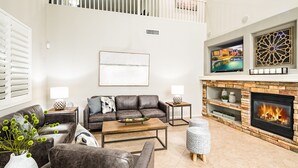 A modern living room with a fireplace, leather sofas, a coffee table, and a TV mounted on the wall. - Prime Location, Heated Pool, Fun Game Room, Putting Green, Outdoor BBQ, & More (Phoenix)