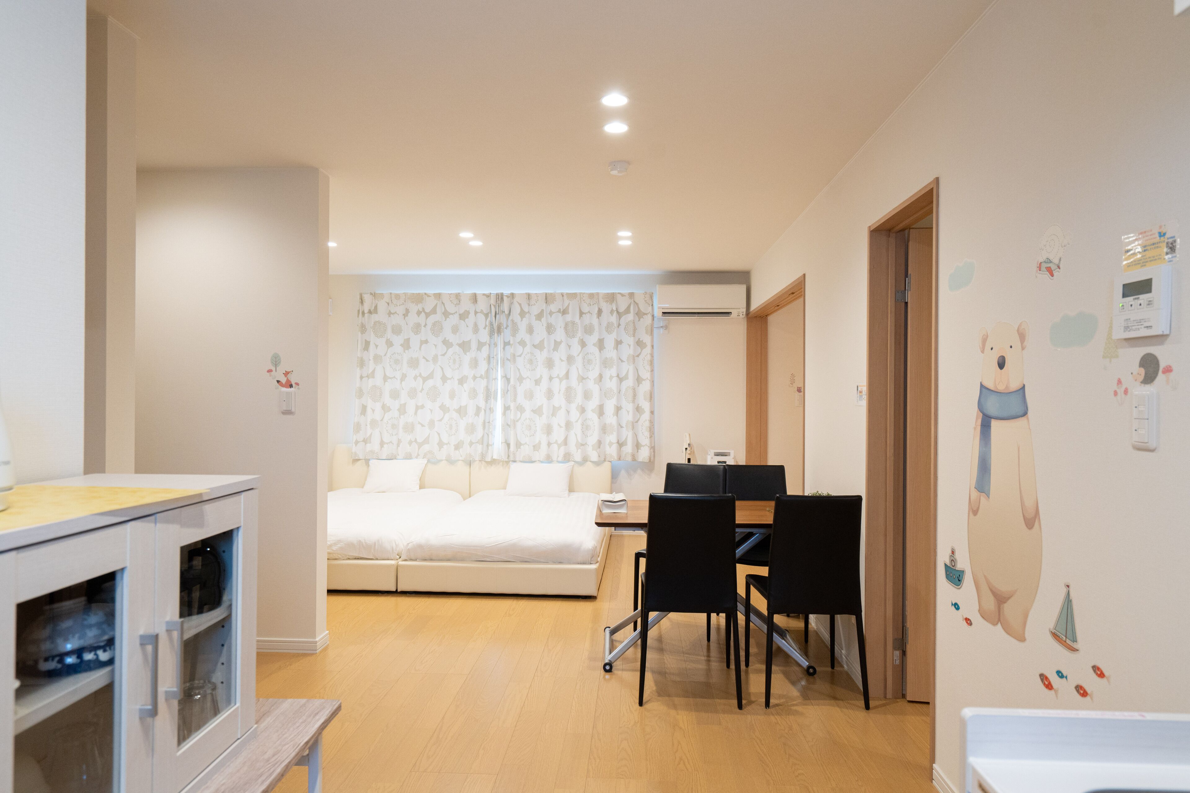 Habitación de hotel moderna con cama, escritorio y silla. Se ve una ventana con cortinas, un equipo de aire acondicionado y una pared decorada con un oso.