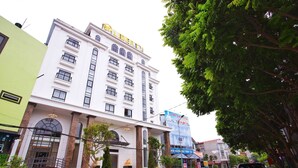 A multi-story hotel with a prominent sign, a staircase leading to the entrance, and a street view with cars and trees. - Liberty Hotel - Events (Lao Cai)