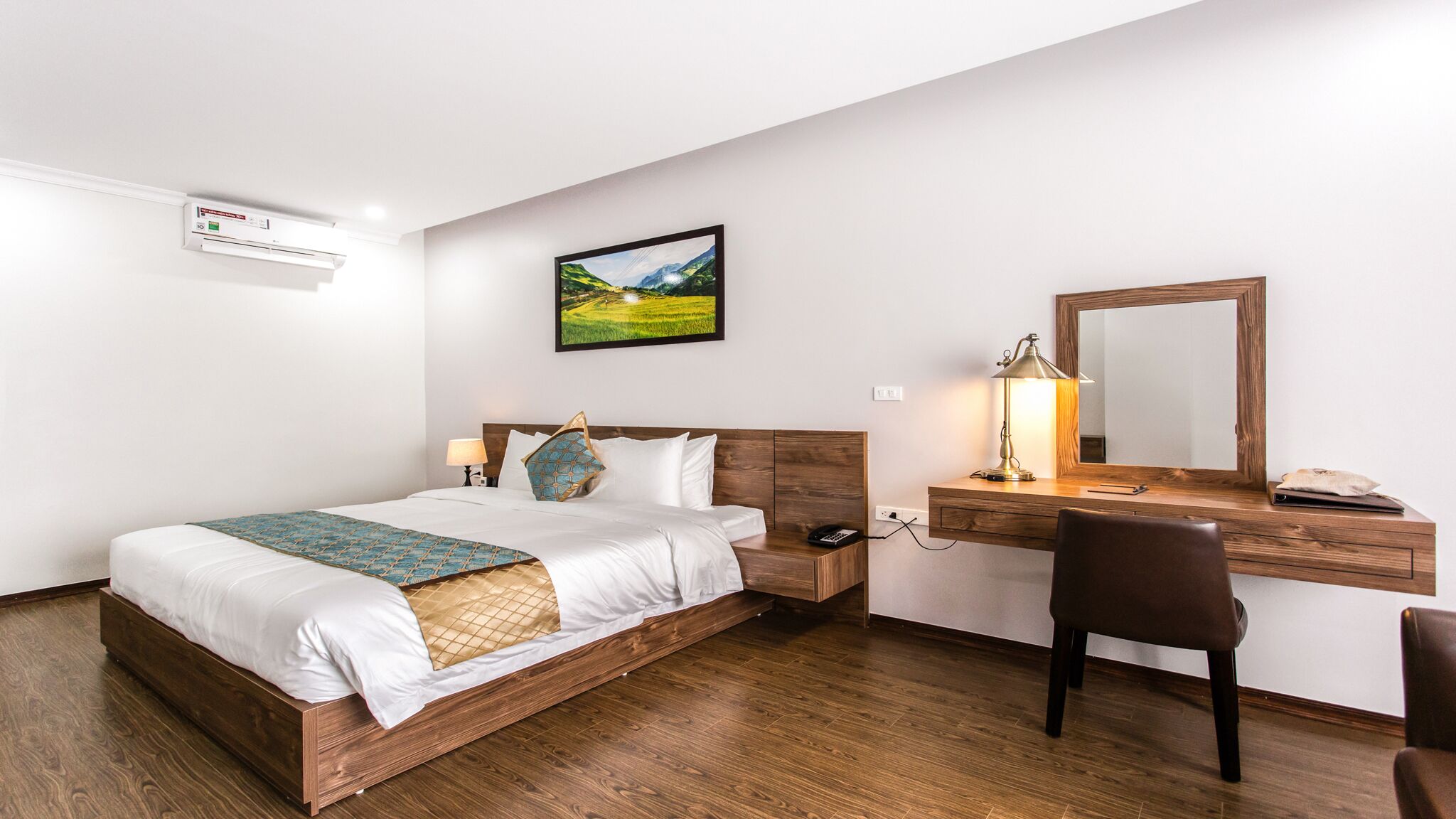 A hotel room with a wooden bed, a desk with a mirror, and a painting on the wall.