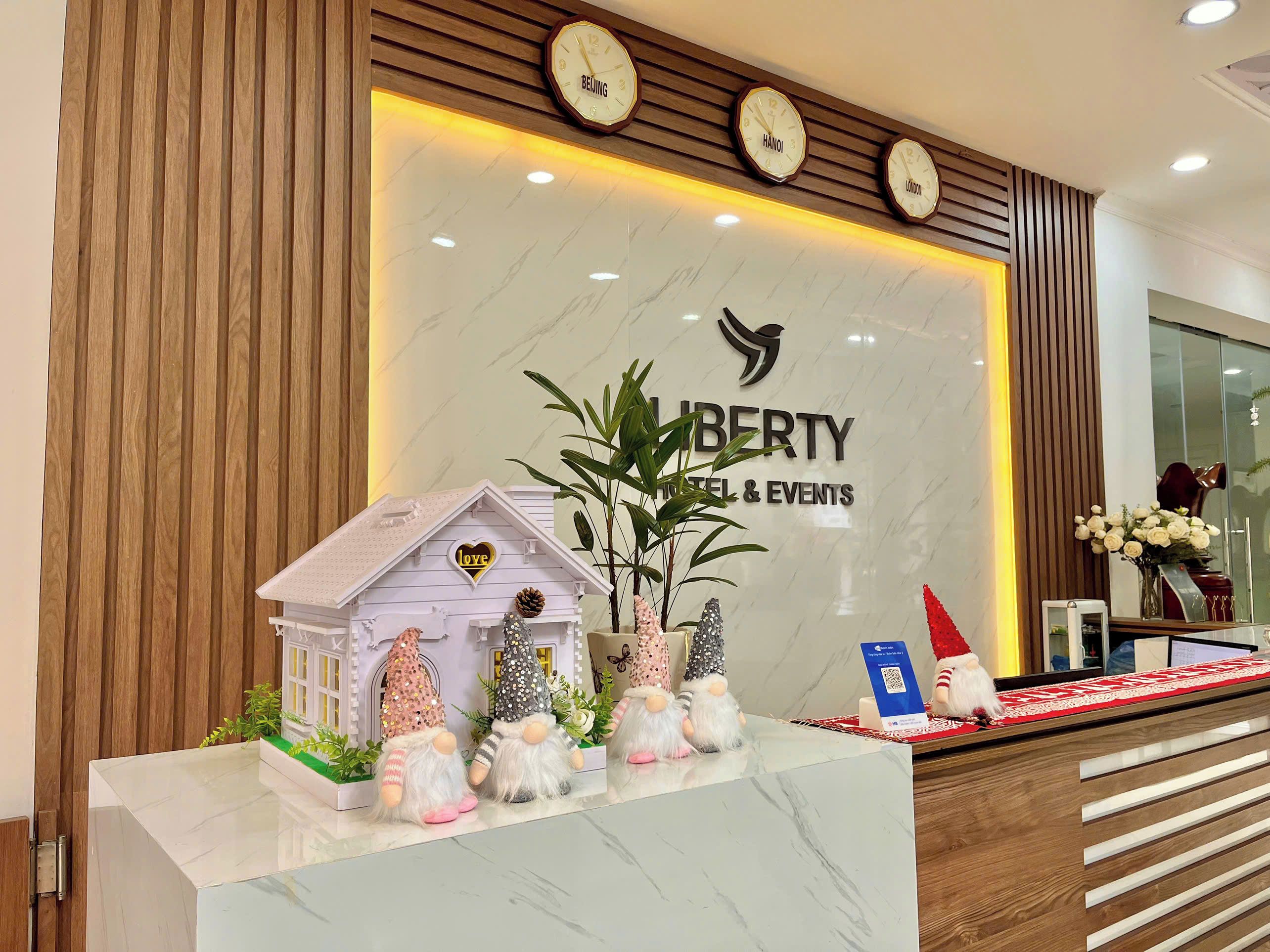 A hotel reception desk with a clock, a sign for 'Liberty Hotel & Events', and decorative gnomes.