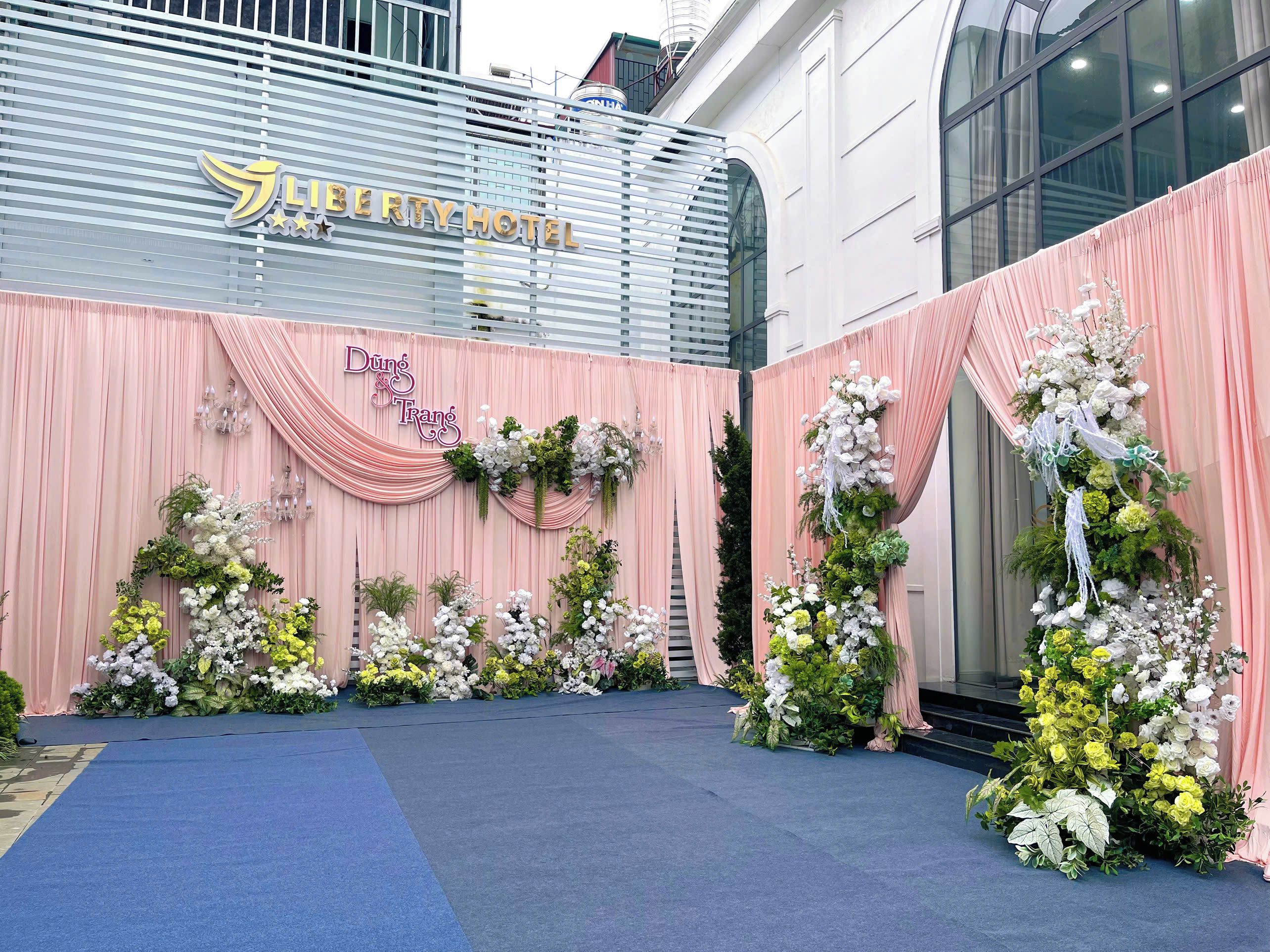A hotel entrance with a blue carpet leading to a stage decorated with flowers and draped curtains.