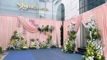 A hotel entrance with a blue carpet leading to a stage decorated with flowers and draped curtains.