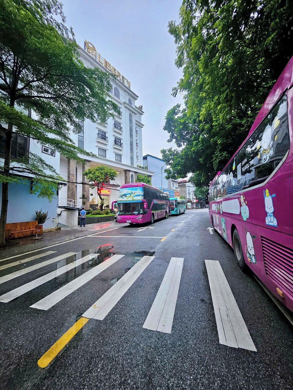 A street with multiple buses parked on the side, a pedestrian crossing, and buildings with commercial establishments.