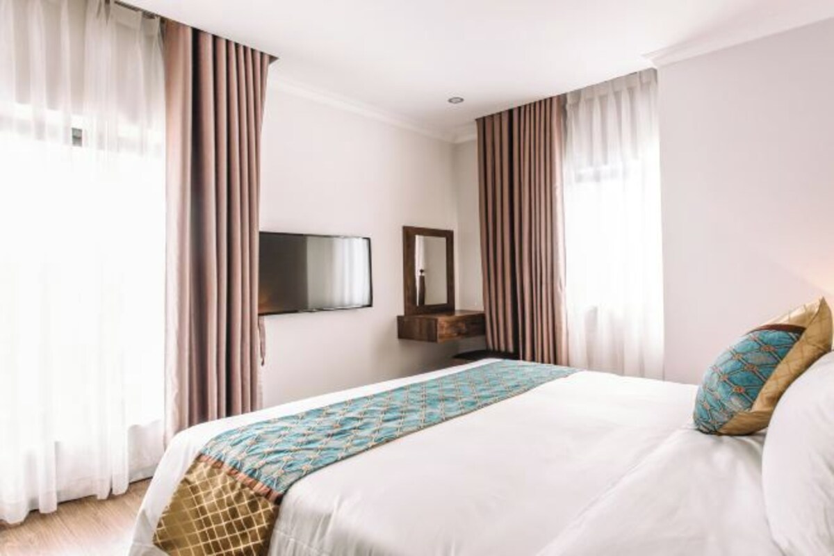 Une chambre d’hôtel avec un lit, des rideaux, une télévision, un miroir et une fenêtre.