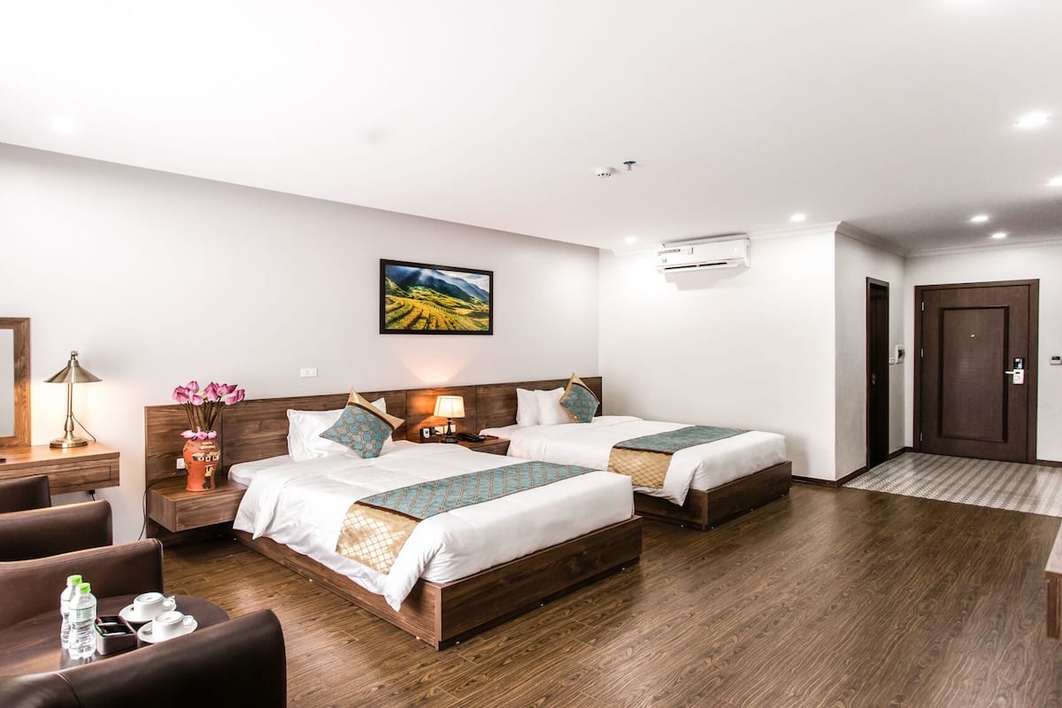 A hotel room with two beds, a desk, a chair, a mirror, and a painting on the wall.