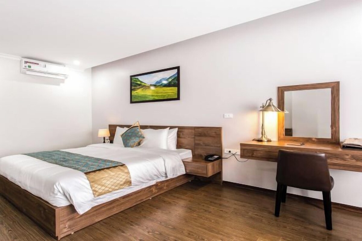 A bedroom with a wooden bed, a desk with a mirror, and a landscape painting on the wall.