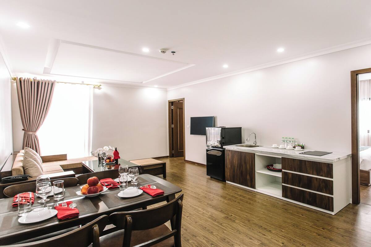 A modern hotel room with a dining area, kitchenette, and a bed.