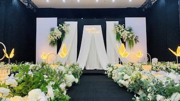 A stage with a black backdrop, white drapery, and floral arrangements.