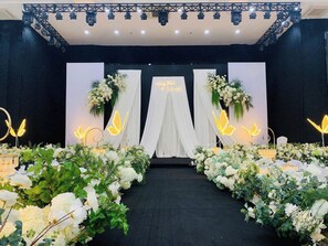 A stage with a black backdrop, white drapery, and floral arrangements. - Liberty Hotel - Events (Lao Cai)