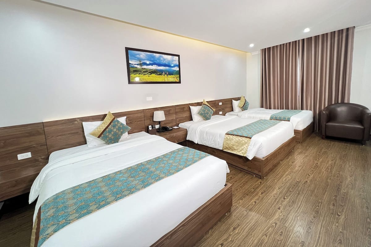 A hotel room with two beds, a nightstand, a lamp, a chair, and a picture on the wall.