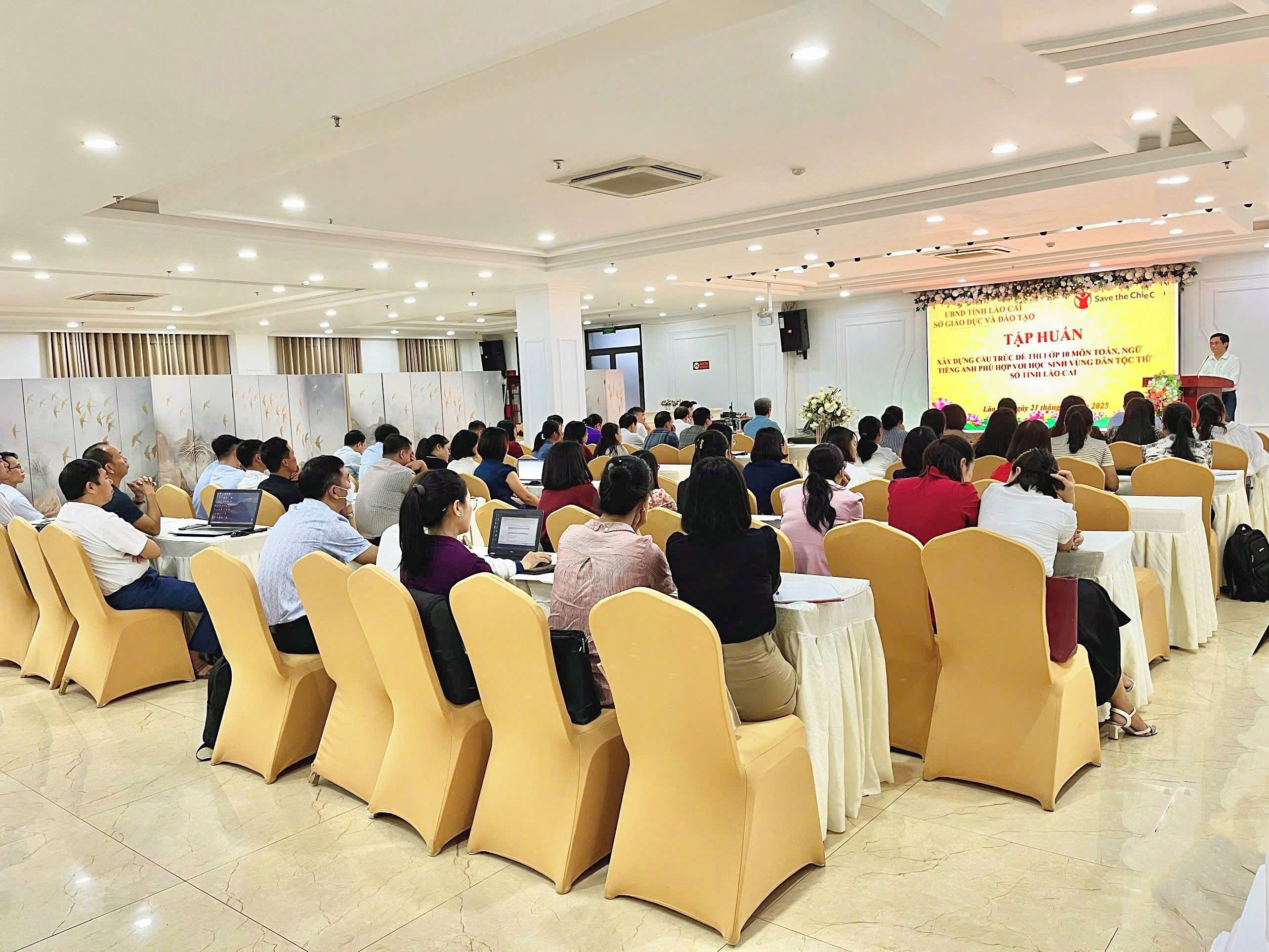 A conference room with attendees seated at round tables, a stage with a speaker, and a banner with text.