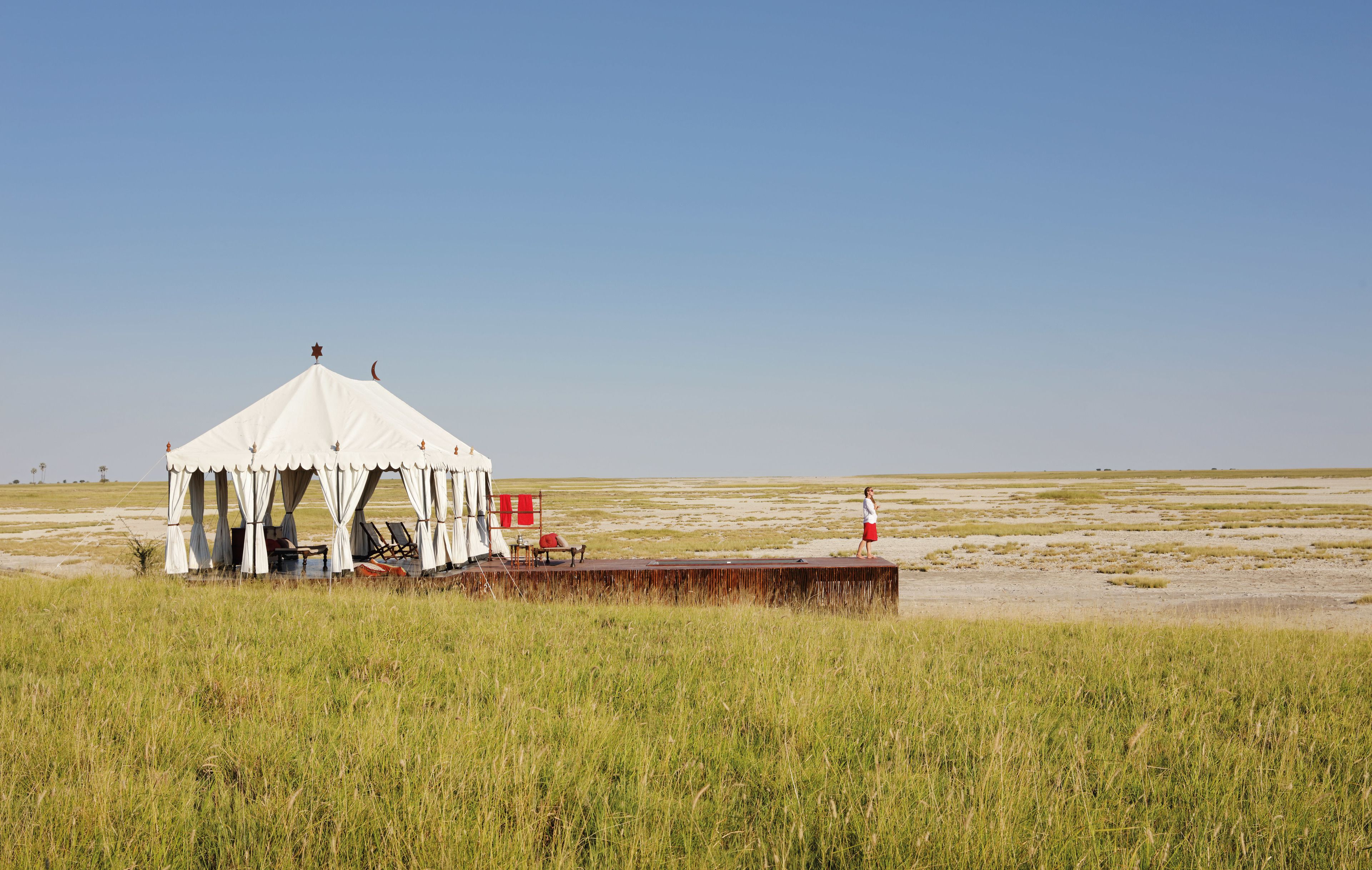 A tent with a platform and seating area, set in a grassy field with a clear sky.
