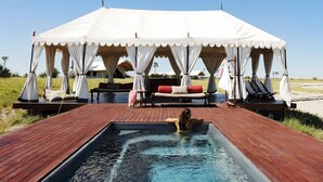 A tented area with a pool and lounge chairs. - San Camp (Central Kalahari Game Reserve)