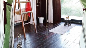 A tented room with a wooden floor, a ladder, a bucket, and a small table with bottles. - San Camp (Central Kalahari Game Reserve)