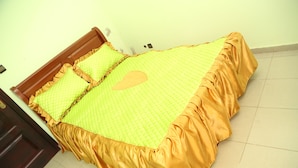 Un lit avec une couette jaune et des volants orange sur les bords, une tête de lit en bois et un mur sobre avec un interrupteur.