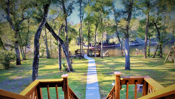 A wooden deck leading to a grassy area with a view of a lake and trees. - Escape to Serenity at Suwannee River Rest – Pet-Friendly Lodge in North Florida (Branford)