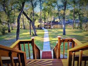 A wooden deck leading to a grassy area with a view of a lake and trees.