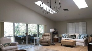 A spacious living room with a large window, a chandelier, a sofa, a chair, and a coffee table. - Escape to Serenity at Suwannee River Rest – Pet-Friendly Lodge in North Florida (Branford)