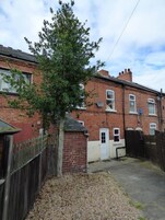 A brick house with a small front yard, a wooden fence, and a tree.