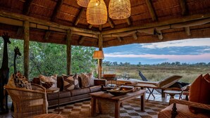 Amplia zona de estar al aire libre con techo de paja, amueblada con sofás, sillones y una mesa de comedor.