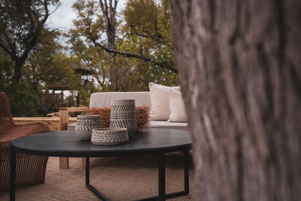 A round table with four patterned ceramic bowls, a wicker chair, a sofa with cushions, and a tree trunk in the foreground.