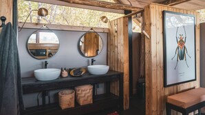 Un baño rústico con dos lavabos, un espejo, un banco de madera y un cuadro con una ilustración de insectos.