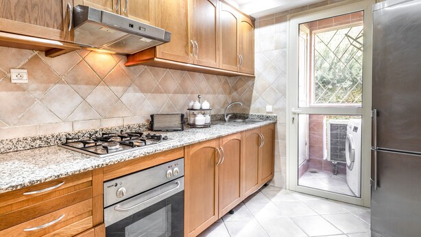 A kitchen with wooden cabinets, a gas stove, a built-in oven, a stainless steel refrigerator, and a window with a view of the outside. - Residence Majorelle Piscine (Marrakech)