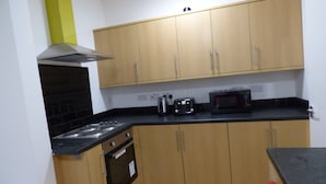 A compact kitchen with wooden cabinets, a black countertop, a stove, a microwave, and a toaster. - PearTree House (Derby)