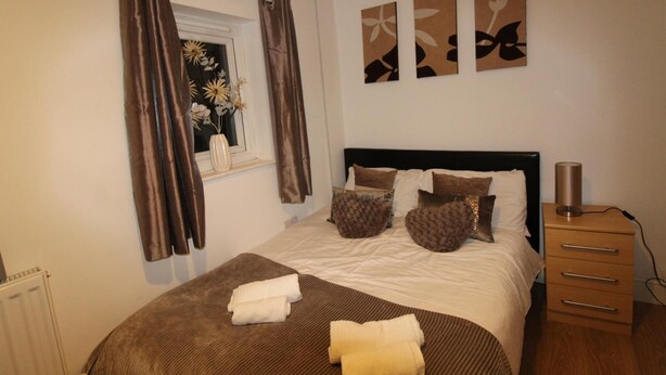 A neatly made bed with a brown headboard, a window with curtains, and three wall art pieces. - PearTree House (Derby)
