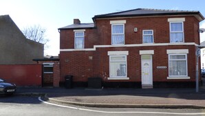 A two-story brick house with a white door and windows, a satellite dish, and a visible street name sign. - PearTree House (Derby)
