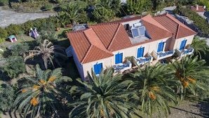 A two-story building with a red-tiled roof, blue-framed windows, and a balcony with a white railing. - Casa Kounopetra (Kefalonia)